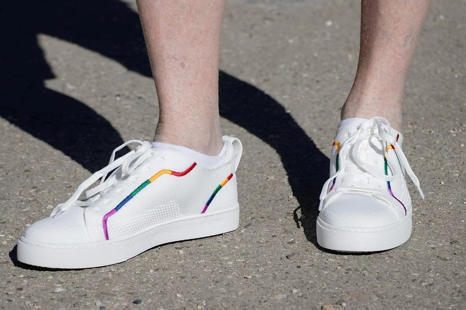 Pair of white sneakers with colourful stripes being worn.